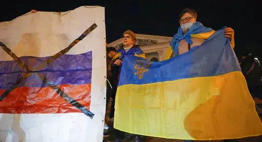 Ukrainians hold up their country's flag, right, as they attend a patriotic action "Mariupol is Ukraine" in Mariupol, Ukraine, Tuesday, Feb. 22, 2022. Europe braced for further confrontation Wednesday, Feb. 23, 2022, after tensions over Ukraine escalated dramatically when Russian President Vladimir Putin got the OK to use military force outside his country and the West responded with sanctions. (AP Photo/Sergei Grits, File)