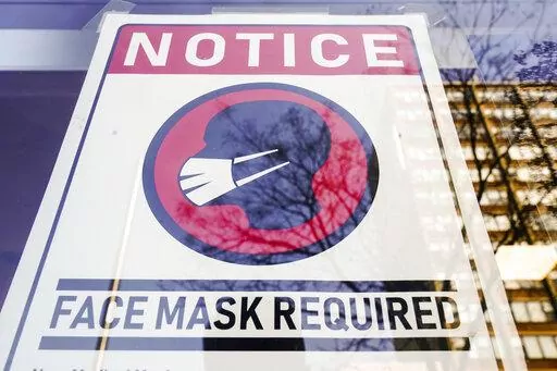 A sign requiring masks as a precaution against the spread of the coronavirus on a store front in Philadelphia, is seen Feb. 16, 2022. Philadelphia is reinstating its indoor mask mandate after reporting a sharp increase in coronavirus infections, Dr. Cheryl Bettigole, the city's top health official, announced Monday, April 11, 2022. Confirmed COVID-19 cases have risen more than 50% in 10 days, the threshold at which the city's guidelines call for people to wear masks indoors. (AP Photo/Matt Rourk