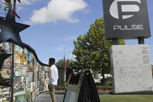 Brandon Wolf, a survivor of the Pulse nightclub shooting and activist, looks at the photos that are a part of the Pulse memorial in Orlando, Fla., on Sept. 9, 2022. (AP Photo/Cody Jackson, File)