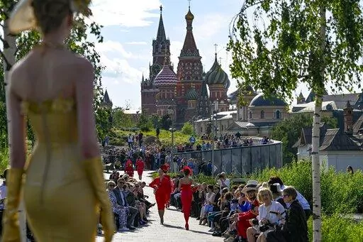 A model displays the collection by Russian designer Slava Zaitsev during the opening of the Fashion Week in at Zaryadye Park with the Spasskaya Tower and St. Basil's Cathedral in the background near Red Square in Moscow, Russia, Monday, June 20, 2022. Chic and adventurous models and couturiers have been spread all over the Russian capital for Moscow Fashion Week, flaunting their designs in venues ranging from a sprawling Stalin-era propaganda exposition to a large park near the Kremlin admired f