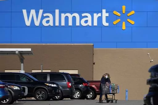 In this Nov. 18, 2020 file photo, a woman wheels a cart with her purchases out of a Walmart store, in Derry, N.H. The holiday season is here, which means spending time with family on Thanksgiving and hunting for the best deals on Black Friday. The term “Black Friday” was linked to a financial crash in the late 1800s and became associated with shopping the day after Thanksgiving in the mid-1900s. A number of stores will be closed on Thanksgiving, including Walmart and Target. (AP Photo/Charle