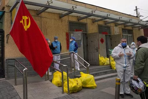 Community workers outside a locked down community chat near a Communist Party flag and trash bags labelled as hazardous waste on Thursday, March 17, 2022, in Beijing. Even as authorities lock down cities in China's worst outbreak in two years, they are looking for an exit ramp from what has been a successful but onerous COVID-19 prevention strategy. (AP Photo/Ng Han Guan)