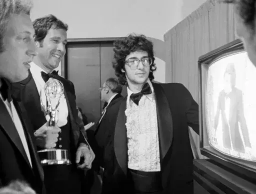 Chevy Chase, a cast member on "Saturday Night Live," holds his Emmy Award as he watches a monitor showing producer Lorne Michaels accepting another Emmy for the show, while writers Alan Zweibel, left, and Tom Davis, right, look on, during the 28th Primetime Emmy Awards in Los Angeles on May 17, 1976. (AP Photo/Reed Saxon, File)