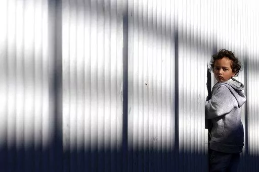 A young migrant stands by a fence at an entry point for asylum seekers Wednesday, Dec. 21, 2022, in Tijuana, Mexico. Thousands of migrants gathered along the Mexican side of the southern border Wednesday, camping outside or packing into shelters as they waited for the U.S. Supreme Court to decide whether and when to lift pandemic-era restrictions that have prevented many from seeking asylum. (AP Photo/Marcio Jose Sanchez)