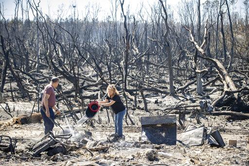Hector Rivera and Wandi Blanco put water on hotspots behind their home in Panama City, Fla., Saturday, March 5, 2022, following a wildfire that started Friday. The fire destroyed two homes next to them and melted the siding off of their home. (Mike Fender/News Herald via AP)