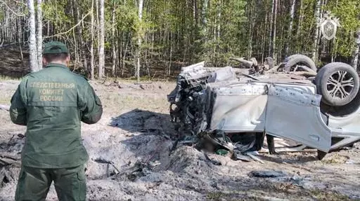 This image taken from video released by the Russian Investigative Committee on Saturday, May 6, 2023, shows a Russian Investigative Committee employee working at the site of the exploded car of Russian writer and publicist Zakhar Prilepin in the region of Nizhny Novgorod, about 400 kilometers (250 miles) east of Moscow. Russian state news agency Tass says the car of Prilepin exploded on Saturday, injuring him and killing his driver. (Russian Investigative Committee via AP)