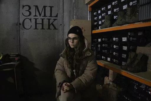Co-founder Kseniia Drahaniuk of the nonprofit group Zemliachky pauses during an interview in front of shelves stacked with military boots at its supply room in Kyiv, Ukraine, on Tuesday, Dec. 6, 2022. The home-grown association helps equip women soldiers who have joined Ukraine's army by the thousands in response to Russia's invasion nearly 10 months ago. (AP Photo/Vasilisa Stepanenko)