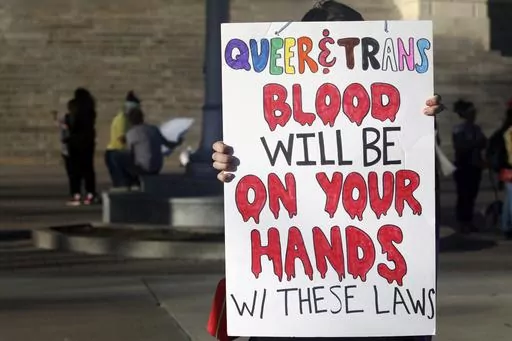 A protester outside the Kansas Statehouse holds a sign after a rally for transgender rights on the Transgender Day of Visibility, March 31, 2023, in Topeka, Kan. Kansas will no longer change transgender people's birth certificates to reflect their gender identities, the state health department said Friday, Sept. 15, 2023, citing a new law that prevents the state from legally recognizing those identities. (AP Photo/John Hanna, File)