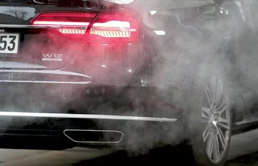 A luxury Audi car is surrounded by exhaust gases as it is parked with a running engine in front of the Chancellery in Berlin, Germany, Wednesday, Nov. 20, 2019. Germany's transport minister said Thursday that he opposes plans to ban the sale of new cars with combustion engines across the European Union in 2035, arguing this would discriminate against vehicles powered with synthetic fuels. EU lawmakers voted Wednesday to back the measure that requires automakers to cut carbon-dioxide emissions by