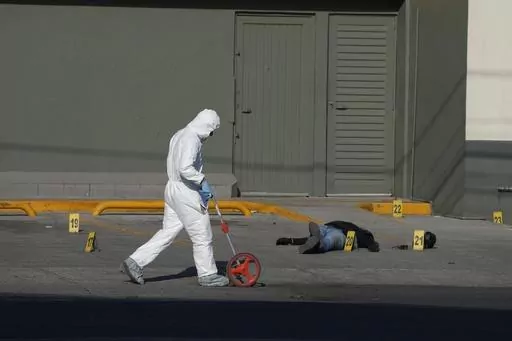 An attacker lies dead on his back in the parking lot of a convenience store as a police investigator uses a measuring wheel while collecting evidence from a crime scene where a municipal policeman was shot dead, in Celaya, Mexico, Feb. 28, 2024. The policeman had been driving his wife to work when cartel gunmen opened fire on their car. The policeman killed one attacker before dying. (AP Photo/Fernando Llano, File)