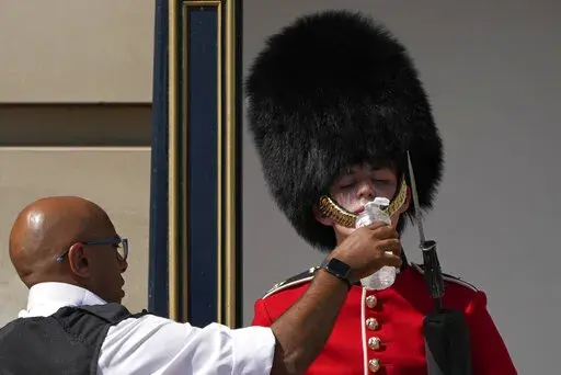 A police officer givers water to a British soldier wearing a traditional bearskin hat, on guard duty outside Buckingham Palace, during hot weather in London, Monday, July 18, 2022. The British government have issued their first-ever "red" warning for extreme heat. The alert covers large parts of England on Monday and Tuesday, when temperatures may reach 40 degrees Celsius (104 Fahrenheit) for the first time, posing a risk of serious illness and even death among healthy people, the U.K. Met Offic