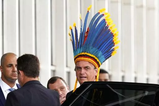 Brazil's President Jair Bolsonaro, wearing a traditional Paresi Indigenous headdress, leaves after participating in a ceremony where he was decorated with the Medal of Indigenous merit, at the Ministry of Justice, in Brasilia, Brazil, March 18, 2022. The accolade scandalized environmentalists, human rights activists and Indigenous groups who see the president’s push for development within Indigenous territories as profoundly damaging. (AP Photo/Eraldo Peres, File)