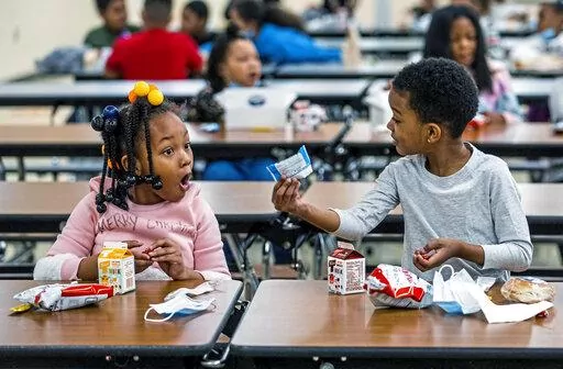 First graders, from left, Kendal Kates and Ryan Kenney are excited about the contents of their boxed lunches at Langley K-8 School, Dec. 23, 2021, in the Sheraden neighborhood in Pittsburgh. The Biden administration has issued transitional standards for school lunches that are meant to get cafeterias back on a healthier course as they recover from pandemic and supply chain disruptions.  The “bridge” rule announced by the U.S. Agriculture Department on Friday extends emergency flexibilities f