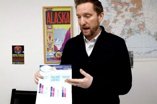 Former Alaska lawmaker Jason Grenn holds an Alaska Division of Elections brochure explaining ranked choice voting at his office in Anchorage, Alaska, on Friday, Jan. 14, 2022. Grenn was sponsor of a ballot initiative passed by Alaska voters in 2020 that would end party primaries and send the top four vote-getters, regardless of party affiliation, to the general election, where ranked-choice voting would determine a consensus winner. The model is unique among states and viewed by supporters as a 