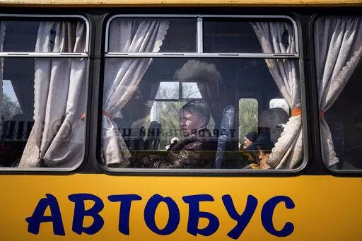 Women wait in a bus at a center for displaced people in Zaporizhzhia, Ukraine, Monday, May 2, 2022. The sign reads: "Bus." (AP Photo/Evgeniy Maloletka)
