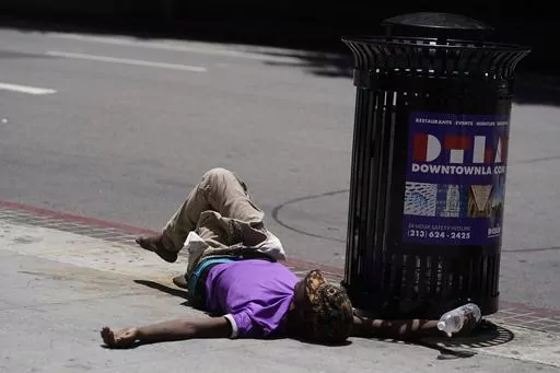 A homeless person lies on the sidewalk while holding a water bottle, Sunday, July 2, 2023, in downtown Los Angeles. Excessive heat warnings remain in place in many areas across the U.S. and are expected to last at least through Monday. (AP Photo/Damian Dovarganes, File)