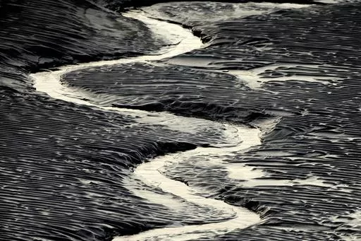 A channel flows through the mud flats along the Seward Highway and Turnagain Arm in Alaska on Oct. 25, 2014. Authorities said, a 20-year-old man from Illinois who was walking Sunday evening, May 21, 2023, on tidal mud flats with friends in an Alaska estuary, got stuck up to his waist in the quicksand-like silt and drowned as the tide came in before frantic rescuers could extract him. (Bob Hallinen/Anchorage Daily News via AP)