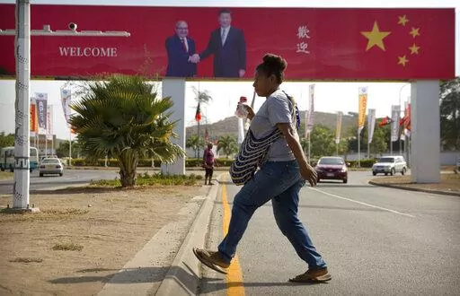 A woman crosses the street near a billboard commemorating the state visit of Chinese President Xi Jinping in Port Moresby, Papua New Guinea, Nov. 15, 2018. China wants 10 small Pacific nations to endorse a sweeping agreement covering everything from security to fisheries in what one leader warns is a “game-changing” bid by Beijing to wrest control of the region. (AP Photo/Mark Schiefelbein, File)