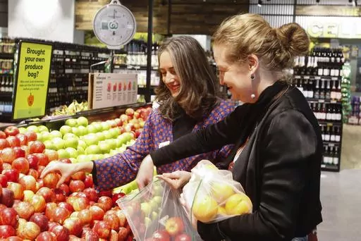 Catherine Langabeer, left, the head of sustainability at the Countdown chain of supermarkets, and Associate Environment Minister Rachel Brooking demonstrate collecting fruit in reusable polyester mesh bags on Thursday, June 29, 2023, at a Countdown supermarket in Wellington, New Zealand. New Zealand's government says that from Saturday, it will be the first nation in the world to ban the thin plastic bags that supermarket customers use to collect their fruit and vegetables. (AP Photo/Nick Perry)