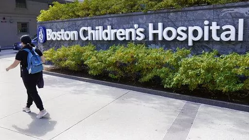 FILE — A woman walks past a sign outside the Boston Children's Hospital, Thursday, Aug. 18, 2022, in Boston. The American Academy of Pediatrics, the American Medical Association and the Children's Hospital Association are asking U.S. Attorney General Merrick Garland to investigate and prosecute people who are threatening violence against children's hospitals and physicians that provide gender-affirming health care. (AP Photo/Charles Krupa, File)
