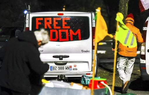 People walk by vehicles with banners and flags parked outside the city center of Brussels, early Monday, Feb. 14, 2022. Authorities in France and Belgium have banned road blockades threatened by groups organizing online against COVID-19 restrictions. The events are in part inspired by protesters in Canada. (AP Photo/Olivier Matthys)