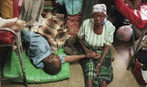 A woman holds the hand of a sick relative lying on the floor of the overcrowded Lilongwe Central Hospital, in Lilongwe, Malawi, Sept. 30, 1998, as the hospital is overflowing because of an epidemic of AIDS rampaging in southern Africa. (AP Photo /Denis Farrell, File)