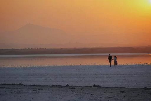A couple walk at the salt lake during sunset in southeast coastal city of Larnaca in southeast Mediterranean island of Cyprus, on Sept. 5, 2022. The eastern Mediterranean and Middle East are warming almost twice as fast as the global average, with temperatures projected to rise up to 5 degrees Celsius (9 degrees Fahrenheit) by the end of the century if no action is taken to reverse the trend, a new report says. (AP Photo/Petros Karadjias, File)