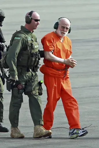 In this June 30, 2011 file photo, James "Whitey" Bulger, right, is escorted from a U.S. Coast Guard helicopter to a waiting vehicle at an airport in Plymouth, Mass., after attending hearings in federal court in Boston. Bulger was fatally beaten at a West Virginia prison in October 2018. An inmate, Paul J. DeCologero, is due in court Thursday, Aug. 1, 2024, for a plea hearing and sentencing on charges in Bulger’s death. (Stuart Cahill/The Boston Herald via AP, File)