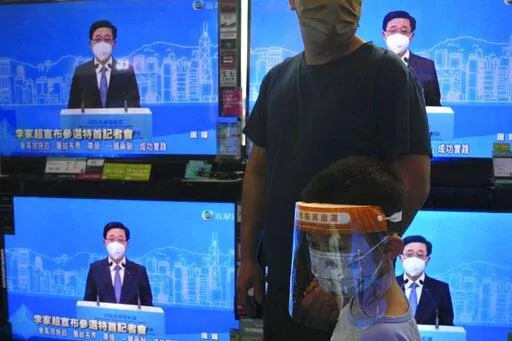 The TV screens show former Hong Kong Chief Secretary John Lee speaks during an online press conference to announce his candidacy for the Election of the Hong Kong chief executive, in Hong Kong, Saturday, April 9, 2022. (AP Photo/Kin Cheung)