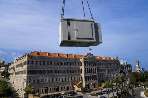 With the Lebanese Government House in the background, a new generator is hauled up to the roof of an office building, in Beirut, Lebanon, Feb. 21, 2022. They literally run the country. Private generators are ubiquitous in parts of the Middle East, spewing hazardous fumes into homes and business across the country, almost 24 hours a day. As the world looks for renewable energy to tackle climate change, Lebanon, Iraq, Gaza and elsewhere rely on diesel-powered private generators just to keep the li