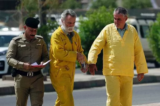 Volker Waldmann, right, and Jim Fitton, center, are handcuffed as they walk to a courtroom in Baghdad, Iraq, Sunday, May 22, 2022. Waldmann and Fitton, accused of smuggling ancient shards out of Iraq, appeared in a Baghdad court Sunday, telling judges they had not acted with criminal intent and had no idea they might have broken local laws. (AP Photo/Hadi Mizban)