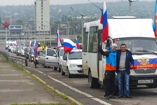 Two men pose for a photo in front of motorcade organized to support voting in a referendum in Luhansk, eastern Ukraine, Friday, Sept. 23, 2022. Voting began Friday in four Moscow-held regions of Ukraine on referendums to become part of Russia. (AP Photo)