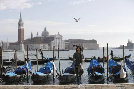 A tourist takes a selfie in St. Mark's Square in Venice, Italy, Nov. 12, 2016. Starting in January, Venice will oblige day-trippers to make reservations and pay a fee to visit the historic lagoon city. On many days, the heart of Venice is overwhelmed by visitors, who often far outnumber residents. Venice officials on Friday unveiled new rules for day-trippers, which go into effect on Jan. 16, 2023. (AP Photo/Luca Bruno, File)