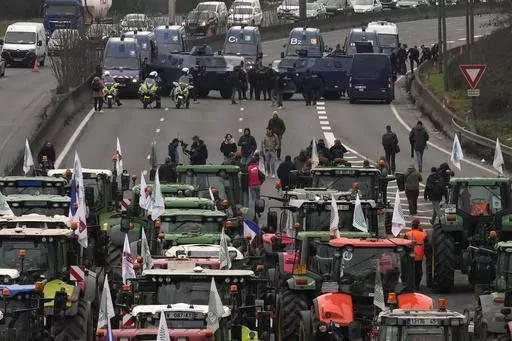Tractors face military vehicles on a blocked highway, Wednesday, Jan. 31, 2024 in Chilly-Mazarin, south of Paris. Farmers have captured France's attention by showering government offices with manure and besieging Paris with traffic-snarling barricades of tractors and hay bales. Protesters say it's becoming harder than ever to make a decent living from their fields, greenhouses and herds. (AP Photo/Thibault Camus)