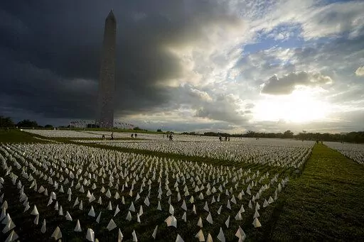 With the Washington Monument in the background, people look at white flags that are part of artist Suzanne Brennan Firstenberg's temporary art installation, "In America: Remember," in remembrance of Americans who have died of COVID-19, on the National Mall in Washington, Sept. 17, 2021. The installation consists of more than 630,000 flags. The federal government has provided more than $2 billion to help cover funeral costs for more than 300,000 families of people who died from COVID-19, the Fede
