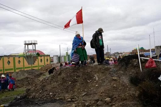 An Aymara woman, holding a Peruvian national, stands on a pile of dirt serving as a roadblock set up by anti-government protesters, in Acora, southern Peru, Jan. 29, 2023. Peruvians have been protesting since early December, when former President Pedro Castillo was impeached after a failed attempt to dissolve Congress. His vice president, Boluarte, immediately took over — and has faced strong opposition ever since. (AP Photo/Rodrigo Abd, File)