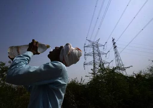 A workers quenches his thirst next to power lines as a heatwave continues to lashes the capital, in New Delhi, India, Monday, May 2, 2022. An unusually early and brutal heat wave is scorching parts of India, where acute power shortages are affecting millions as demand for electricity surges to record levels. (AP Photo/Manish Swarup)