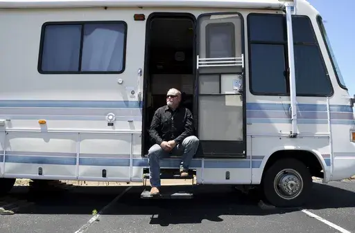 Joe Ridenour sits for a portrait on the steps of the recreational vehicle he once called home in Castle Rock, Colo., on Friday, July 12, 2024. Ridenour said he would have been consumed by his drug abuse if not for the help and shelter provided by The Rock non-denominational evangelical church. (AP Photo/Thomas Peipert)