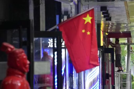 A worker stands on a platform near a Chinese national flag, Friday, July 15, 2022, in Beijing. China's economy contracted in the three months ending in June compared with the previous quarter after Shanghai and other cities shut down to fight coronavirus outbreaks, but the government said a "stable recovery" is under way after businesses reopened. (AP Photo/Ng Han Guan)