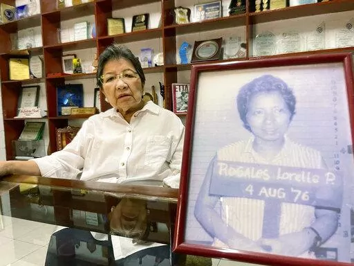 Human rights activist Loretta Rosales sits behind a photo, a grainy military mugshot of her taken after she got arrested in 1976, at her house in Manila, Philippines on Feb. 23, 2022. Memories of the “People Power” revolt by millions of Filipinos who helped overthrow Philippine dictator Ferdinand Marcos 36 years ago are bittersweet for Rosales, who opposed him as an activist and was arrested and tortured by his forces before his downfall. Her battle, however, has gone full circle. The euphor