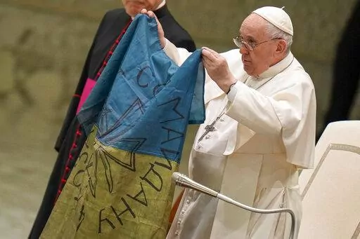 Pope Francis shows a flag that was brought to him from Bucha, Ukraine, during his weekly general audience in the Paul VI Hall, at the Vatican, Wednesday, April 6, 2022. (AP Photo/Alessandra Tarantino)