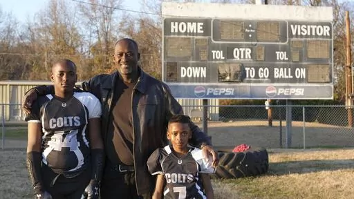 This photo provided by the University of Maryland shows Ronald Redmond standing with sons, 11-year-old R.J., left, and 7-year-old Mason on a football field in Lexington, Mississippi, Jan. 4, 2024. Lexington, Miss. is located in the second-poorest county in the nation’s poorest state. Yet a new analysis shows the town sends more players per capita to elite college football programs than any other town in Mississippi – at a rate that’s among the top in the nation. For many families, the game