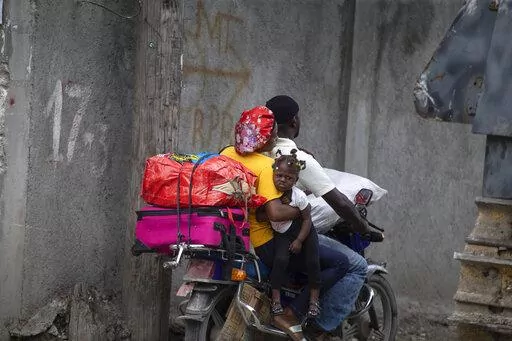 Residents travel on a motorbike as they flee their home to avoid clashes between armed gangs, in the Croix-des-Mission neighborhood of Port-au-Prince, Haiti, Thursday, April 28, 2022. Experts say the scale and duration of gang clashes, the power they are wielding and the amount of territory they control has reached levels not seen before. (AP Photo/Odelyn Joseph)