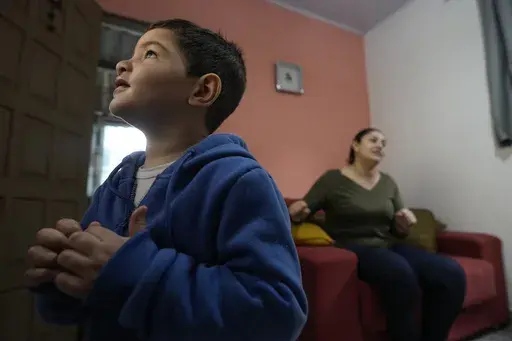 Four-year-old Murillo, who suffers from severe epilepsy, watches TV at his grandparent's home in Guaruja, Brazil, Monday, July 8, 2024. To lessen and shorten his seizures, Murillo takes a steady dose of liquid cannabidiol or CBD, that his mother, pictured in background, acquires for free through Sao Paulo state’s public health system. (AP Photo/Andre Penner)
