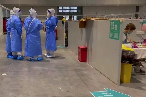 In this image taken from video provided by Beibei, who asked to be identified only by her given name, medical workers wearing protective suits chat as a resident takes a rest at the National Exhibition and Convention Center on April 15, 2022, in Shanghai.  The convention center converted to a quarantine facility set up for people who tested positive but have few or no symptoms. (Beibei via AP)