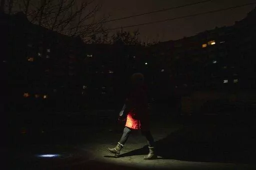 A woman lights up the road with a flashlight during blackout in Kyiv, Ukraine, Friday, Feb. 3, 2023. (AP Photo/Evgeniy Maloletka)
