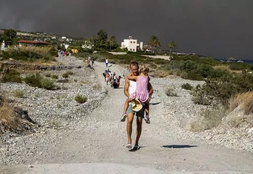 A man carries a child as they leave an area where a forest fire burns, on the island of Rhodes, Greece, Saturday, July 22, 2023. A large wildfire burning on the Greek island of Rhodes for a fifth day has forced authorities to order an evacuation of four locations, including two seaside resorts. (Lefteris Diamanidis/InTime News via AP)
