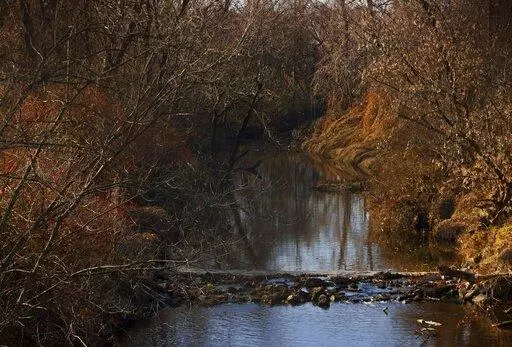 Water flows in Coldwater Creek on Thursday, Dec. 9, 2021, behind a row of homes at Belcroft Drive and Old Halls Ferry Road in Missouri's St. Louis County. Environmental investigation consultants have found significant radioactive contamination at an elementary school, which sits in the flood plain of Coldwater Creek which was contaminated by nuclear waste from weapons production during World War II. (Christian Gooden/St. Louis Post-Dispatch via AP)