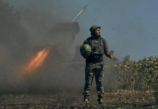 A Ukrainian soldier holds a watermelon and thumbs up as a rocket launch system fires in the font line in Donetsk region, eastern Ukraine, Saturday, Aug. 3, 2022. (AP Photo/Kostiantyn Liberov)