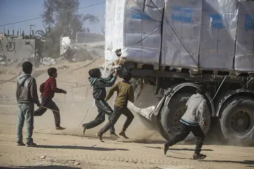 Palestinians chase humanitarian aid trucks that arrived through the Kerem Shalom crossing from Egypt into the Gaza Strip, in Rafah, Tuesday, Jan. 21, 2025. (AP Photo/Jehad Alshrafi)